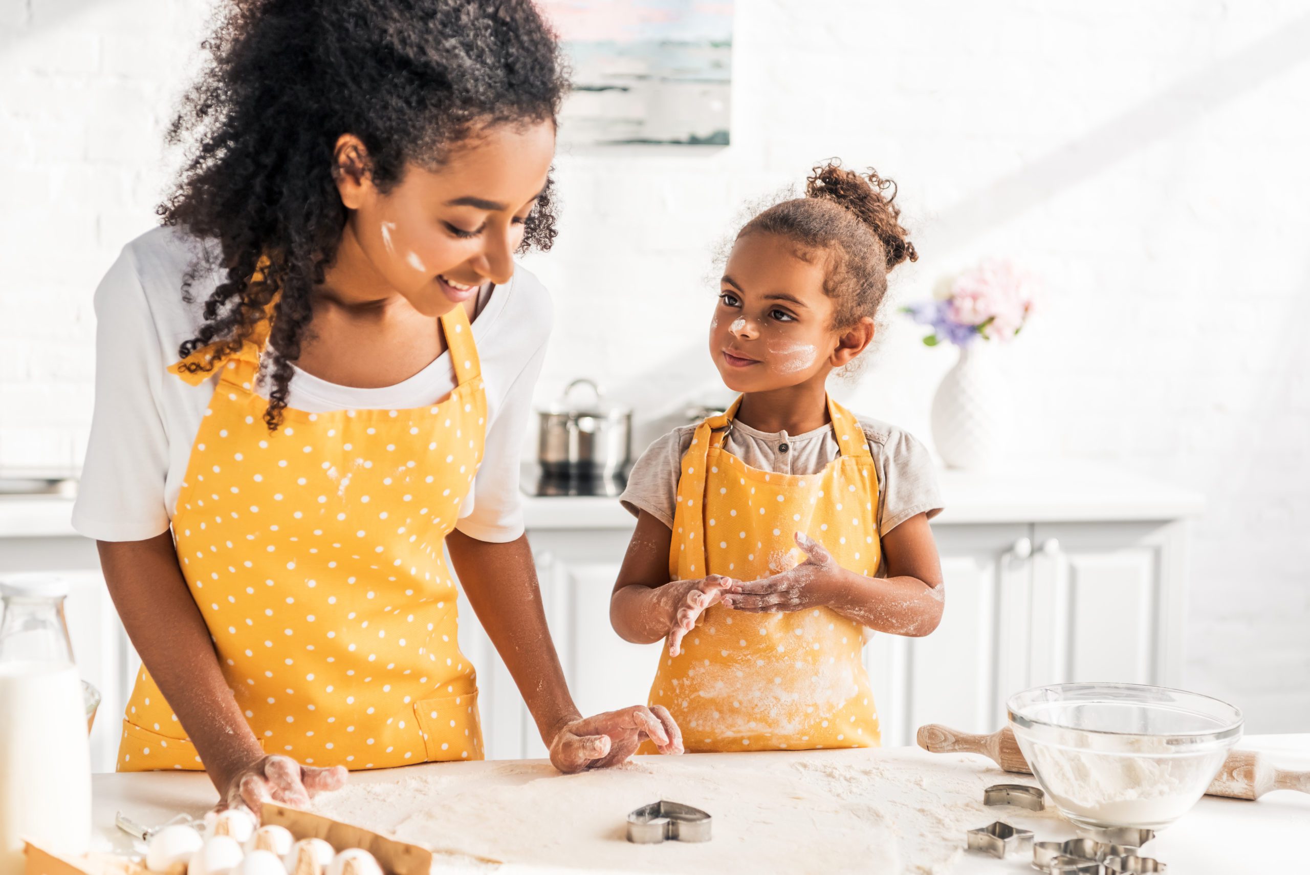 african american mother and daughter preparing cookies with molds together in kitchen