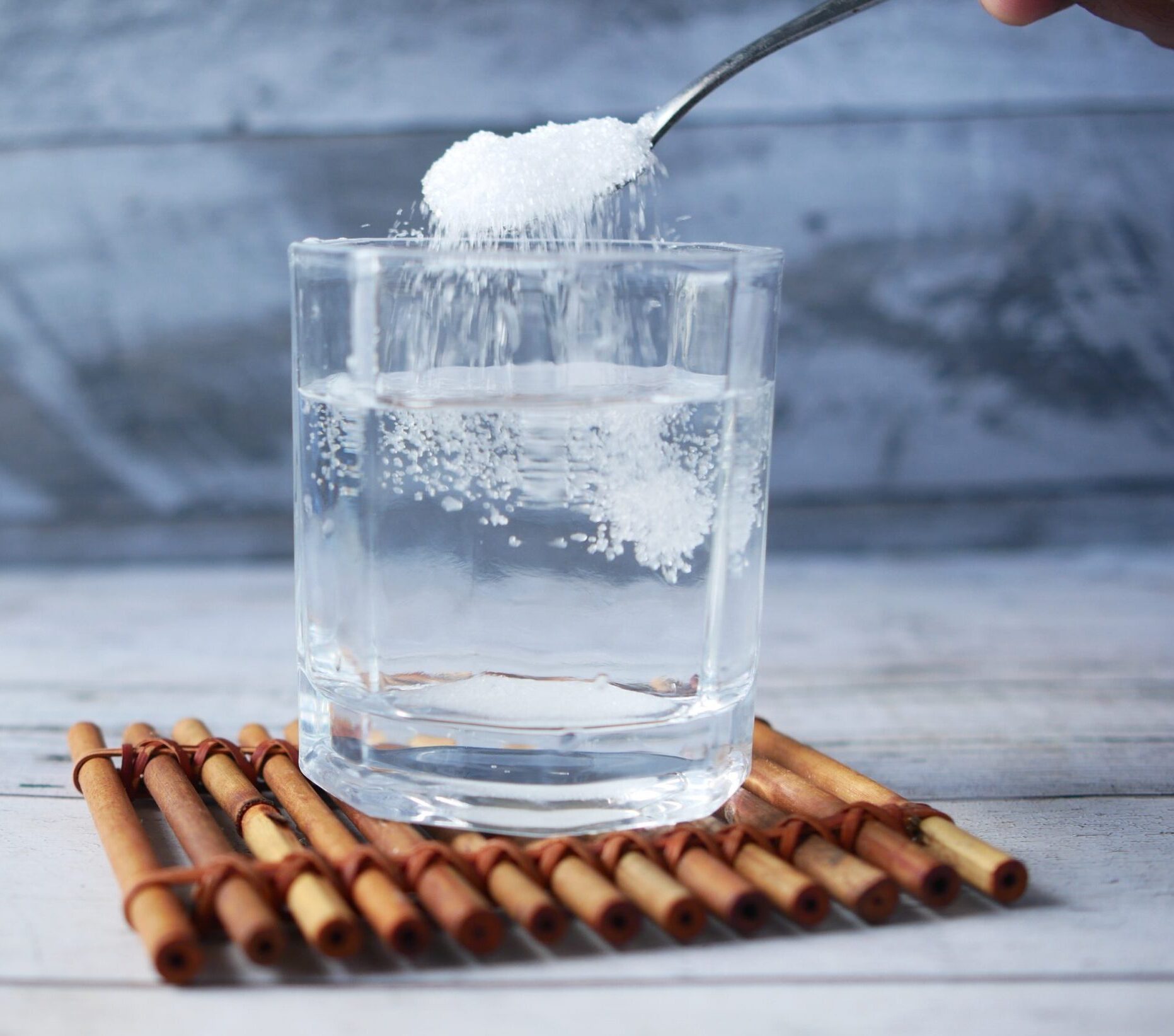 glass of water with sugar being poured into it